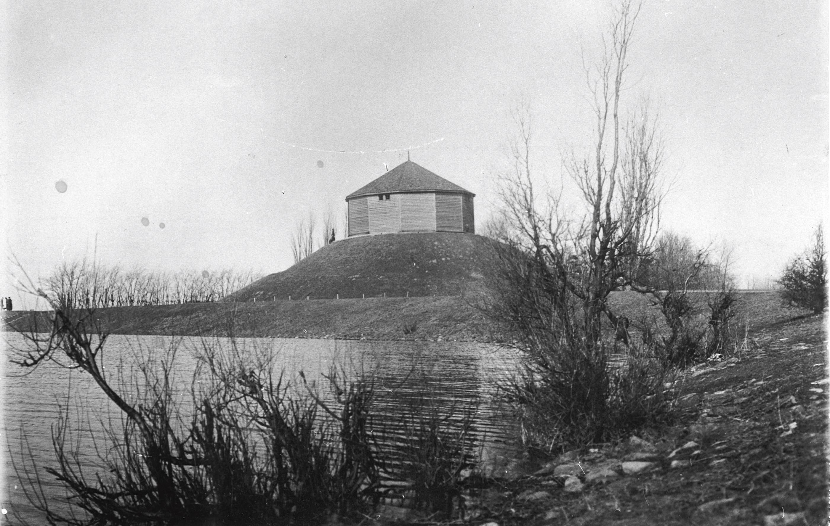 Svartvitt foto på en rund byggnad uppe på en kulle omgiven av vatten.