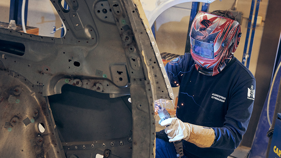 Elev med skyddshjälm svetsar på en karossdel.