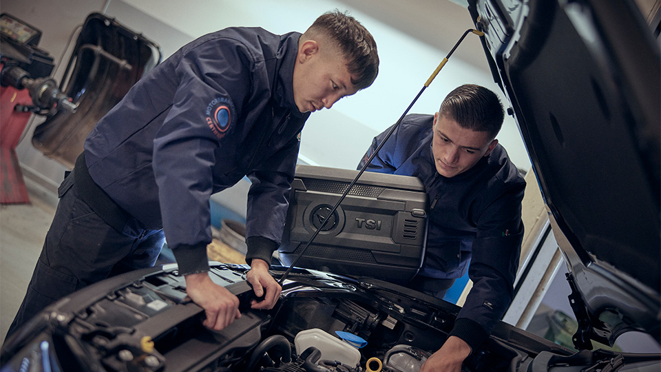 Två elever lutar över en personbilsmotor.
