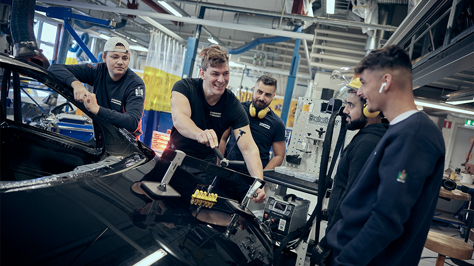 Lärare och fyra elever arbetar vid en motorhuv.