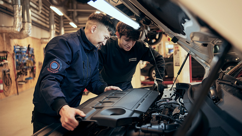 Två elever lutar över en personbilsmotor.