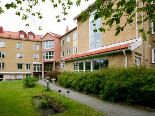 En grusgång som omges av gröna buskar leder fram till det gula tegelhusets ingång på innergården.