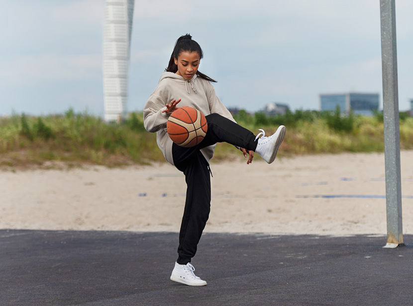 Person dribblar med basketboll på en basketplan. I bakgrunden syns stranden.