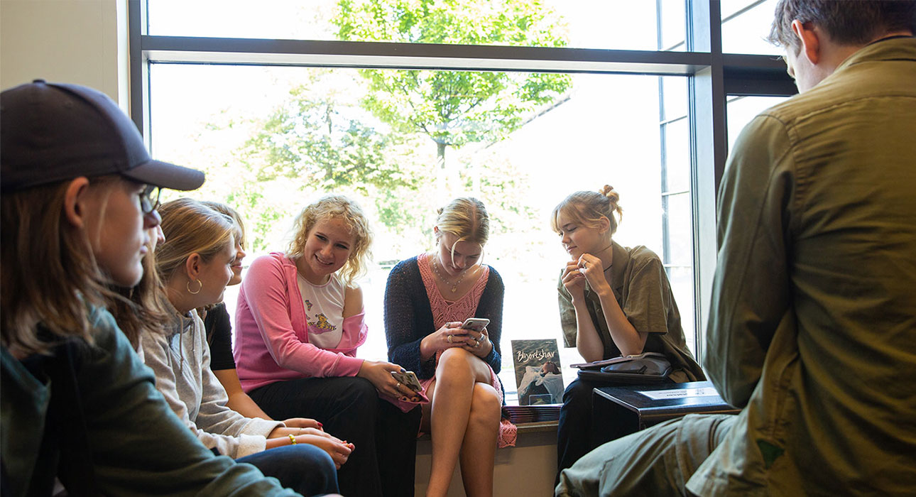 Grupp med elever sitter i soligt fönster i biblioteket.