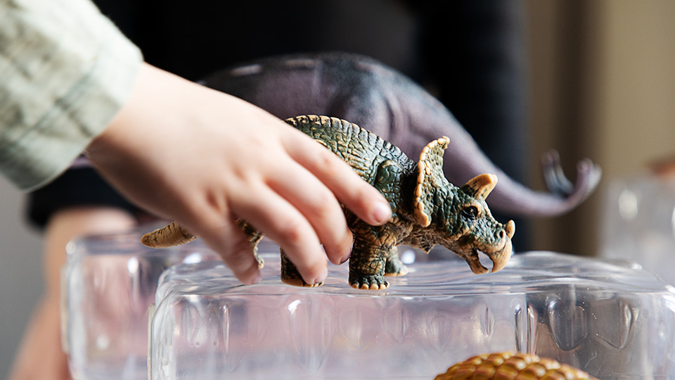 Närbild på en barnhand som håller i en dinosaurie. 