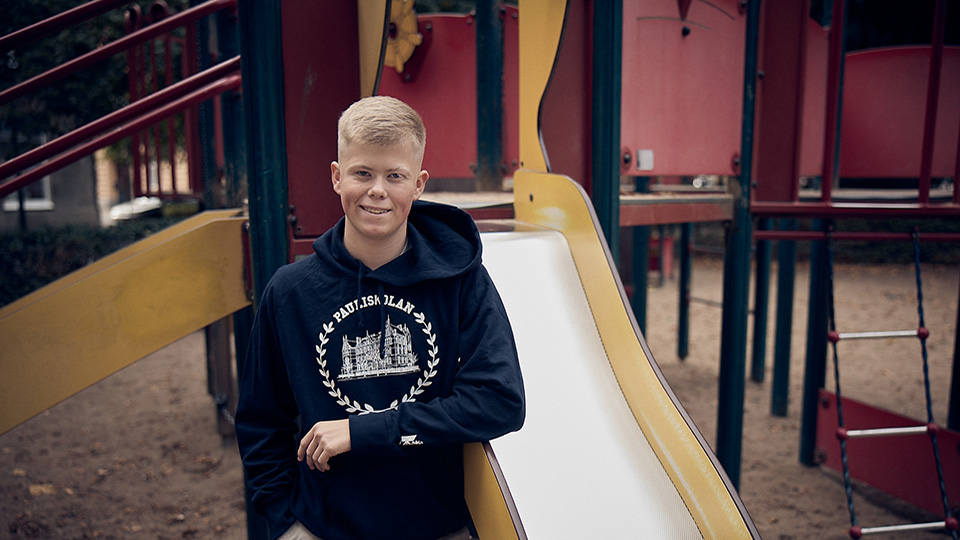 En elev på Barn- och fritidsprogrammet tittat glatt in i kameran. I bakgrunden syns en rutschkana på en lekplats.
