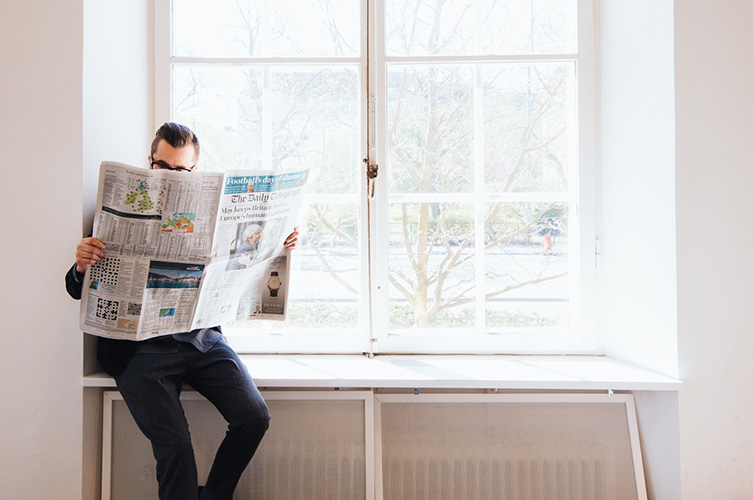 Person sitter i fönsterkarm och läser tidning.