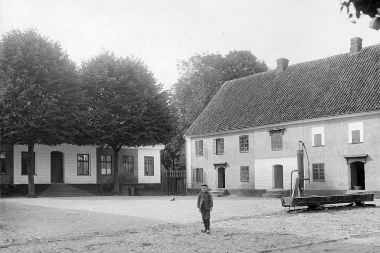 Gammal svartbild bild från gården på Katrinetorp. Mitt på gården står ett barn och tittar mot kameran.