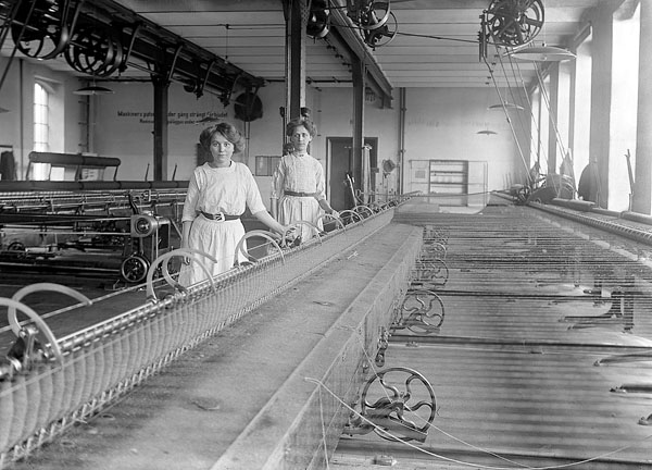 Fotografi på två kvinnor i vita klänningar som står bakom en maskin.
