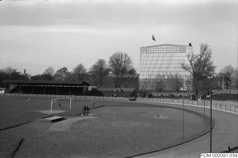 Äldre fotografi över idrottsplatsen som har en stor gräsmatta och en läktare.