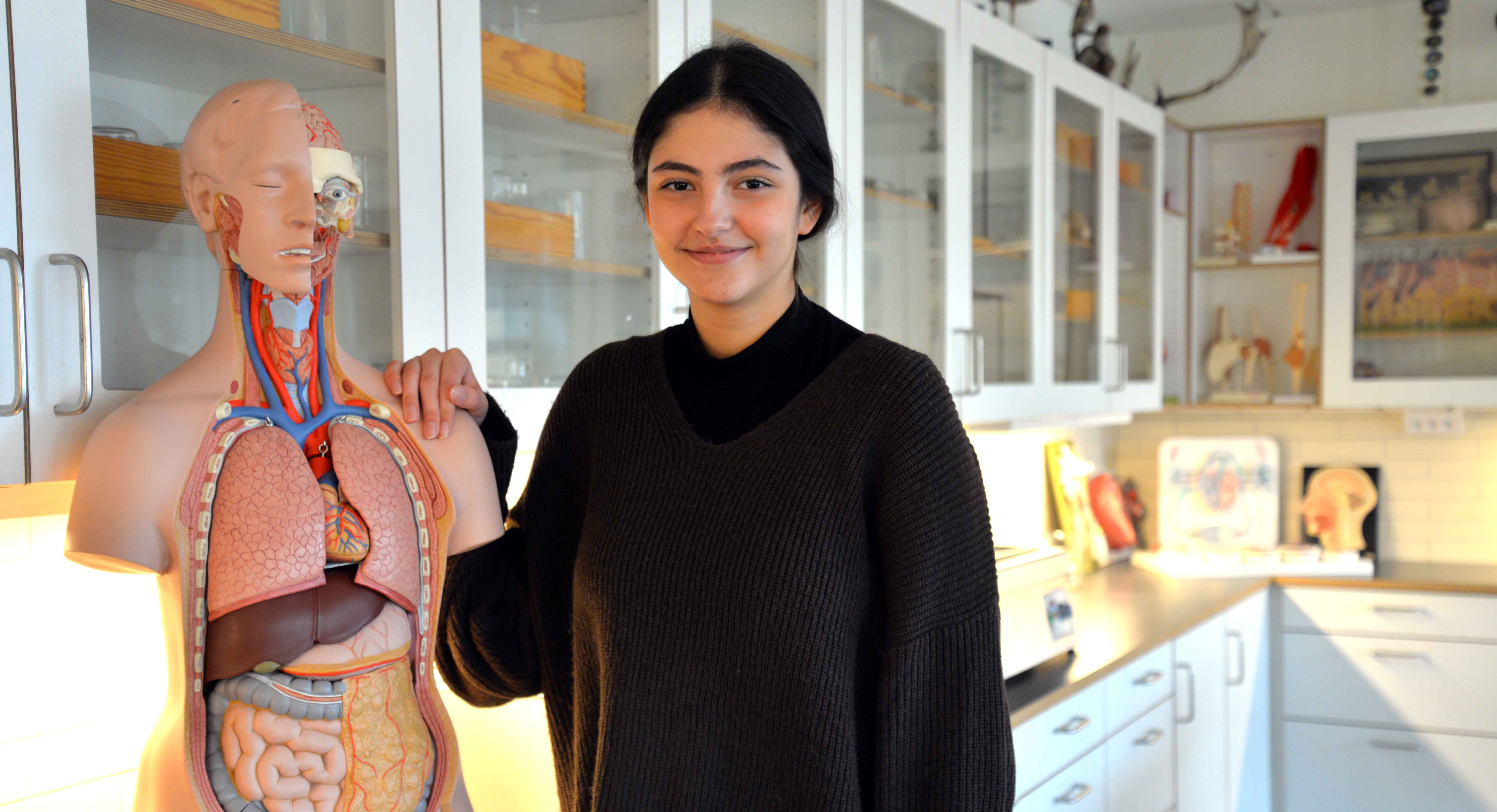 Yasma, elev på Borgarskolan står bredvid en modell av en människokropp i en biologisal.