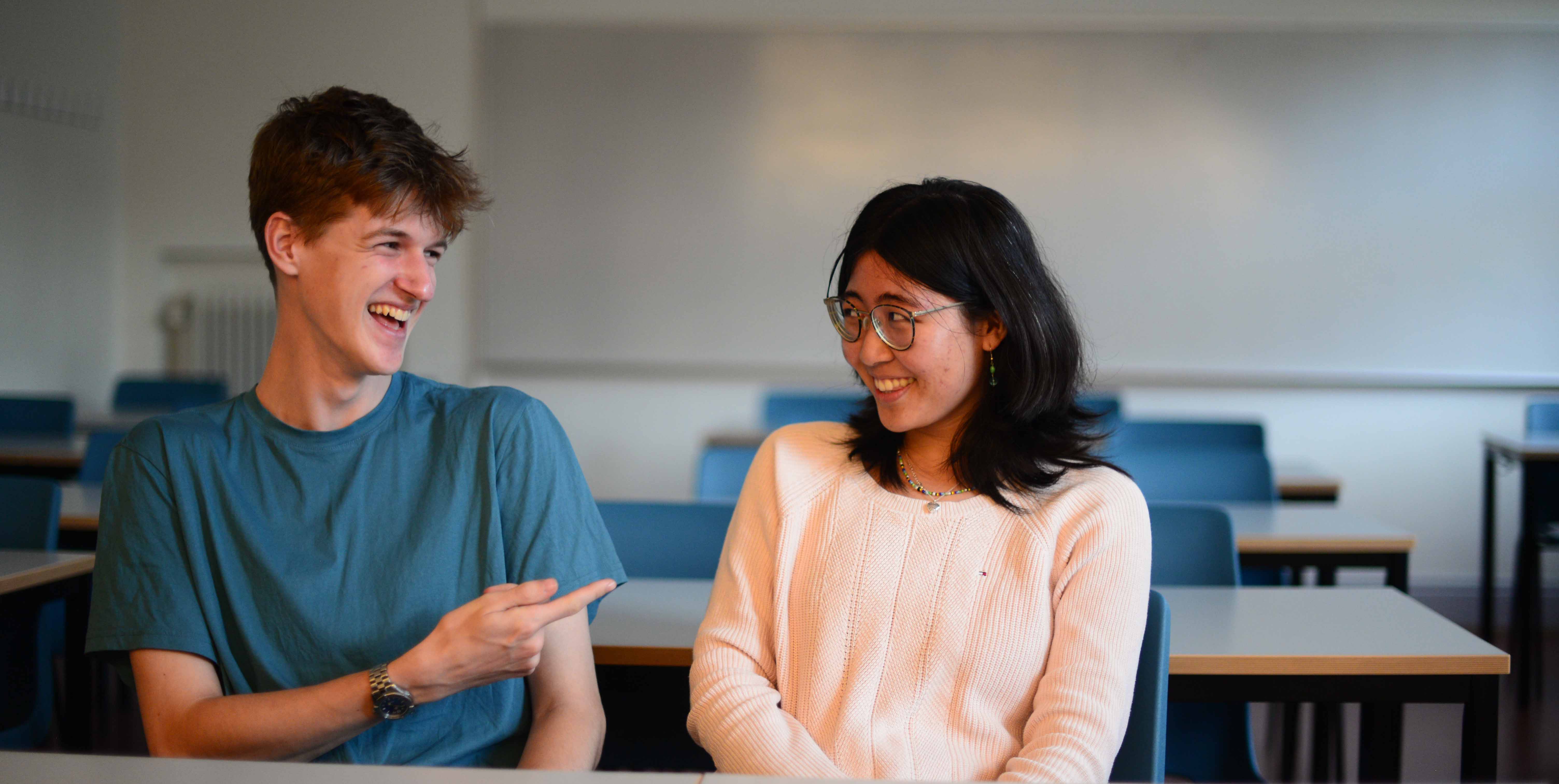 Thomas och Sabrina, elever på Malmö Borgarskola sitter i ett klassrum. Thomas pekar på Sabrina och de skrattar.