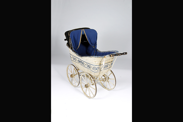 Liggvagn med flätad korg, ekerhjul och
sufflett. Tillverkare: AB A. W. Nilssons Fabriker, Malmö. Vit med blå dekor
samt blått tyg (madrass och gardin). Suffletten löstagbar. Foto: Okänd fotograf
/ Malmö museum.