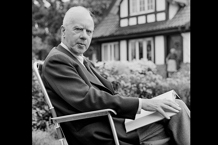 Äldre porträttfoto på Anders Österling. Han sitter med en bok i knät och ser allvarsam ut. Bilden är tagen utomhus i en park eller trädgård.