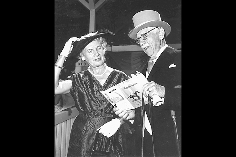 Axel och Eva Cronquist
står högtidsklädda på en träläktare på Jägersro travbana i Malmö och tittar i
ett program 1958. Foto: Okänd fotograf / Malmö Museer.