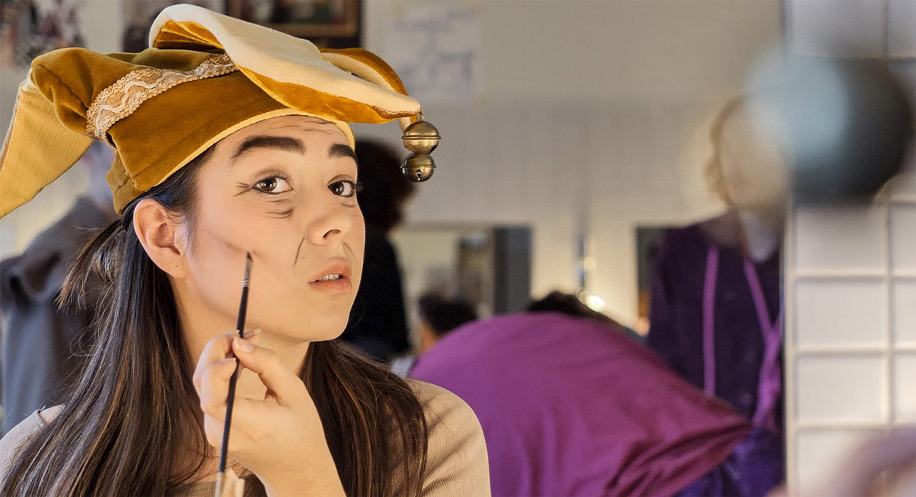 En elev i en teaterloge som sminkar sig framför en spegel.