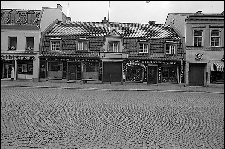 Äldre fotografi på hus vid Djäknegatan, i bottenplan ligger en blomsterbutik. 