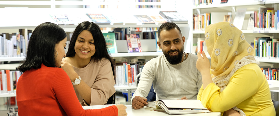 Tre kvinnor och en man har grupparbete i biblioteket.
