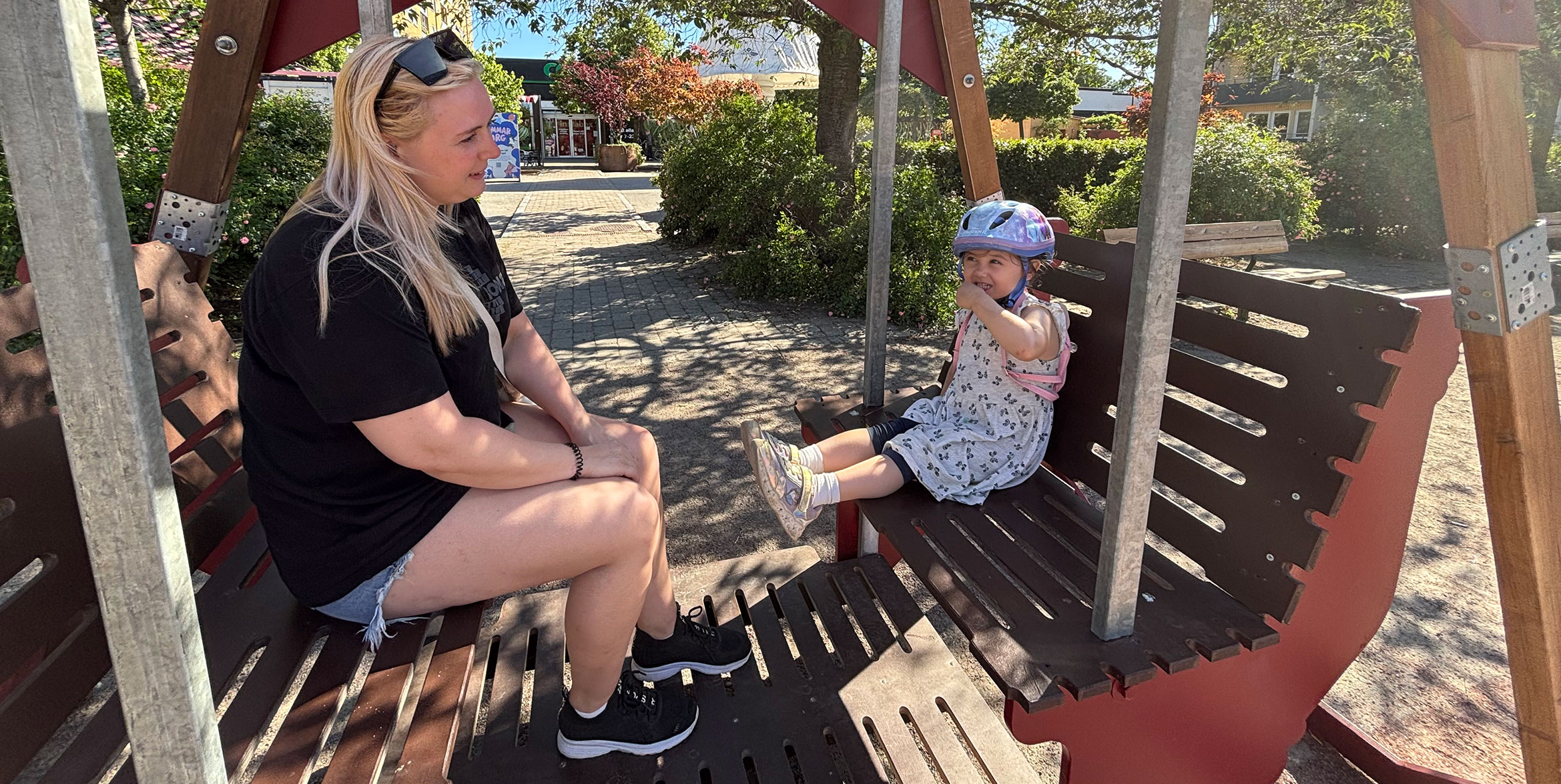 En mamma och en dotter sitter i en hammock på ett torg.