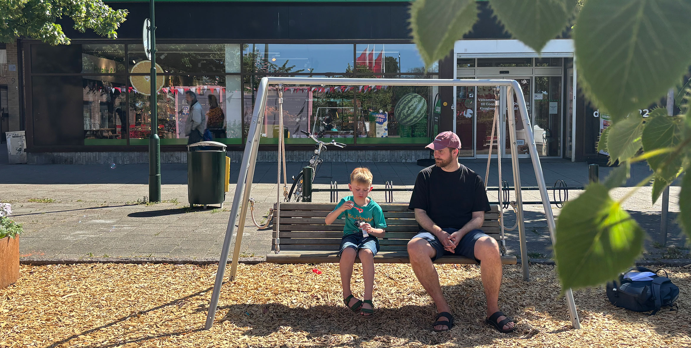 En pappa och en son sitter i en hammock på ett torg.