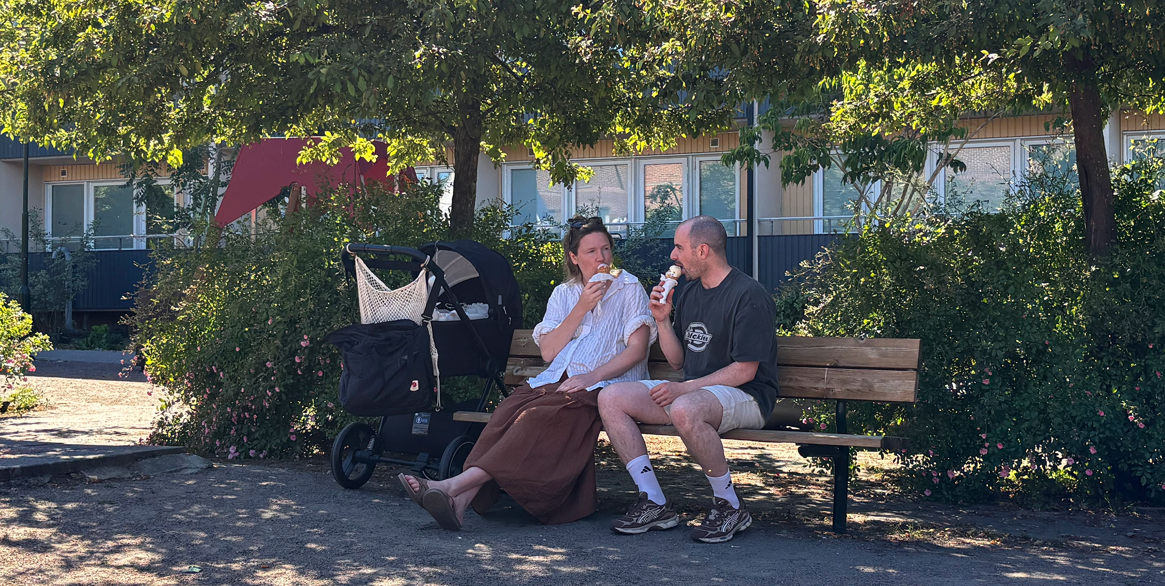 En kvinna och en man sitter på en bänk och äter glass. Bredvid dem står en barnvagn.