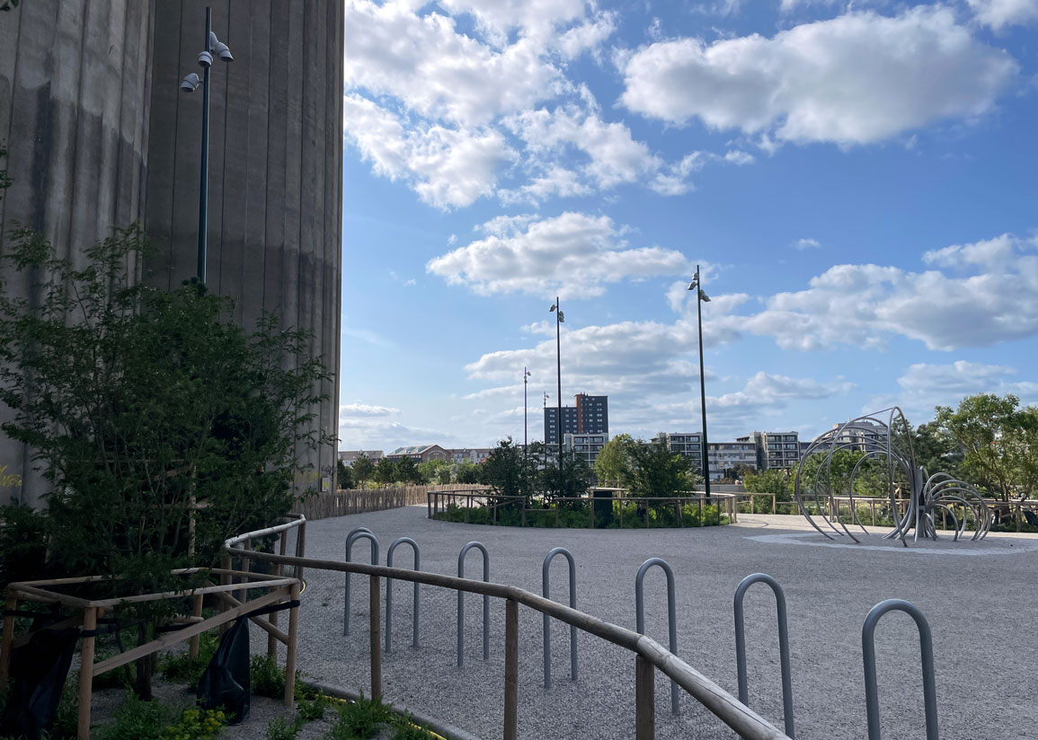 Fendertorget sett från Fendergatan, med cementfabrikens gamla silor som ger skugga. Blå himmel och vita stackmoln, Ön i bakgrunden.
