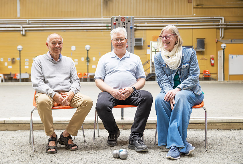 Kenth, Sven och Marika sitter på stolar på boulebanan och ler.