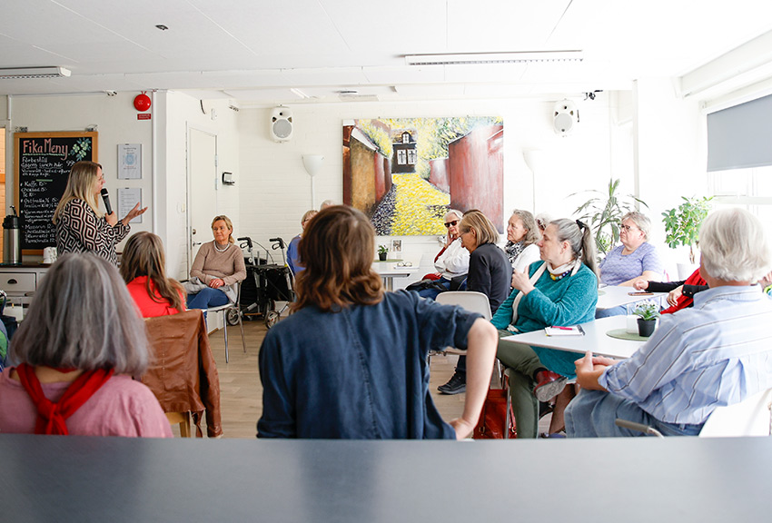 Helen står med en mikrofon framför en grupp med personer på mötesplats Ignis.
