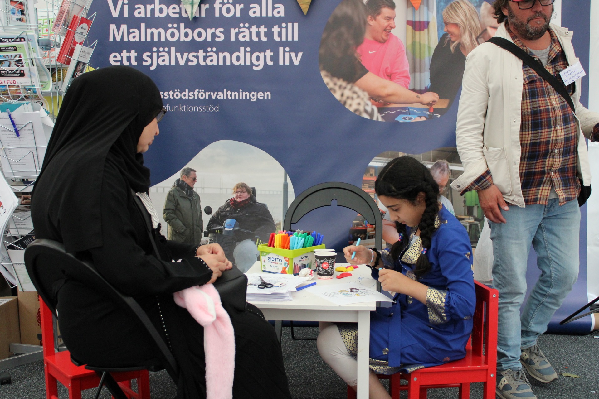 Ett barn och en vuxen sitter vid ett litet bord utanför funktionsrättstältet och pysslar.