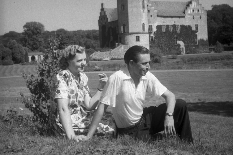 Historisk bild på ett par som sitter på en äng och håller handen