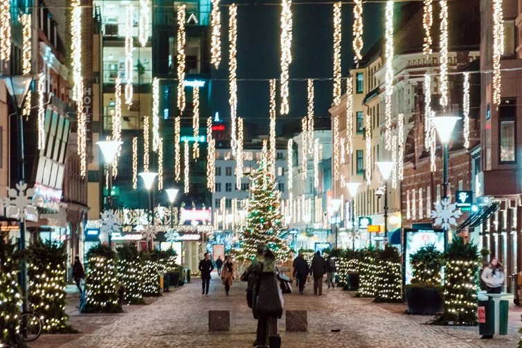 En gågata i centrala Malmö med julbelysning. Olika ljusinstallationer hänger ner över gatan och skapar en stark julstämning.