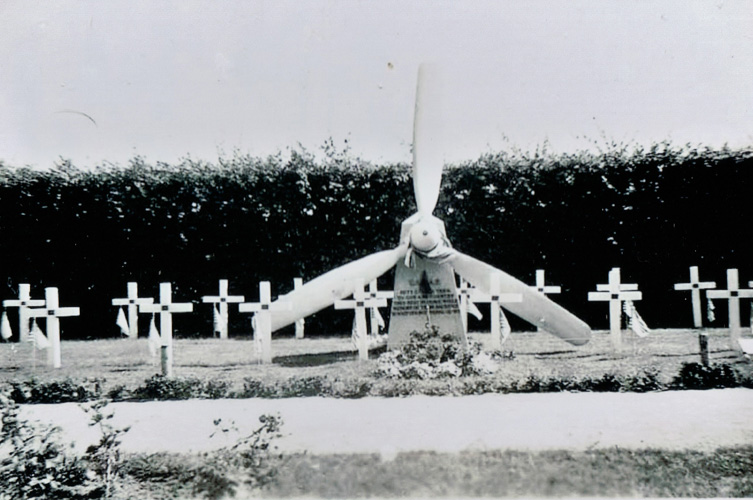 Svartvitt äldre fotografi. På bilden syns en begravningsplats med ett flertal kors. En större gravsten är i centrum, dekorerad med en propeller.