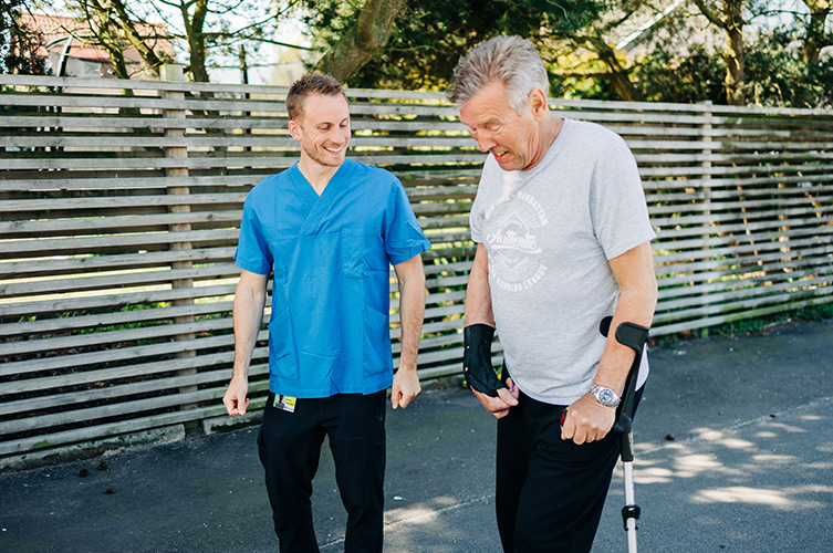 Fysioterapeuten Isak hjälper en man med krycka att gå.