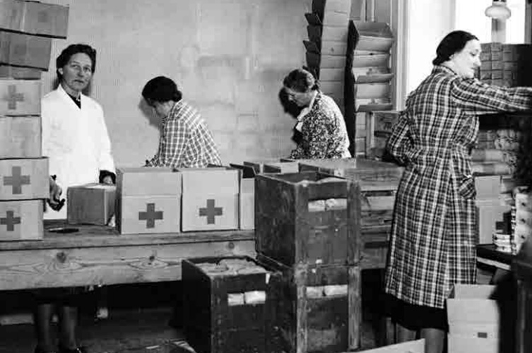 Svartvitt fotografi föreställande kvinnliga hjälparbetare som packar förnödenheter i kartonger. 