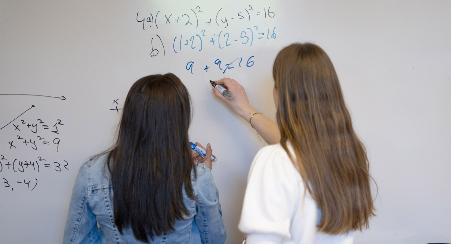 Två elever skriver en matematisk formel på en vittavla.