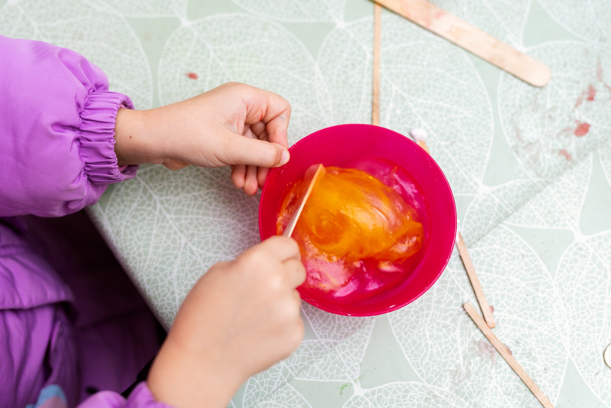 Ett barn rör i en skål med orange, slemmigt pysselmaterial.