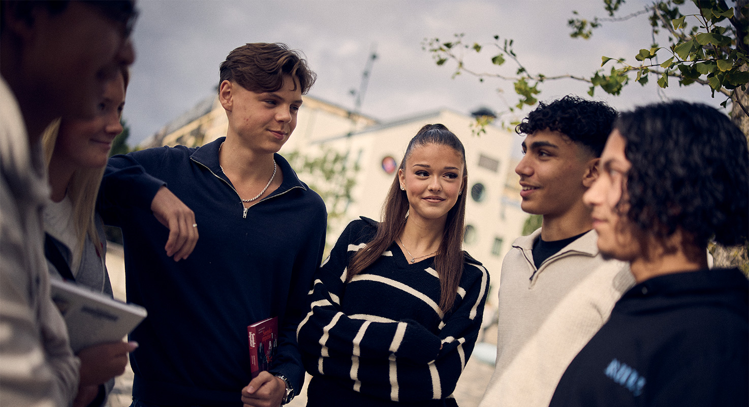 Sex glada elever i en klunga i samtal utanför skolan.
