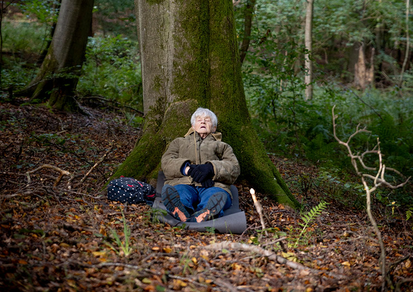 Anne Juhlin sitter vid foten av ett träd och sover.