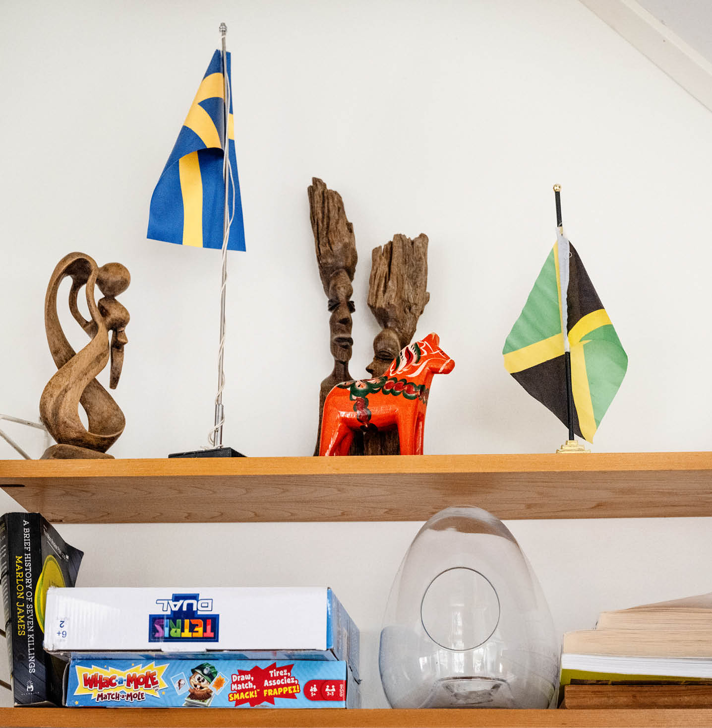 Sniderier i trä står tillsammans på en hylla med
bordsflaggor för den svenska och den jamaicanska flaggan. En dalahäst i
förgrunden. Spel och en ljuslykta står på hyllan nedanför. 