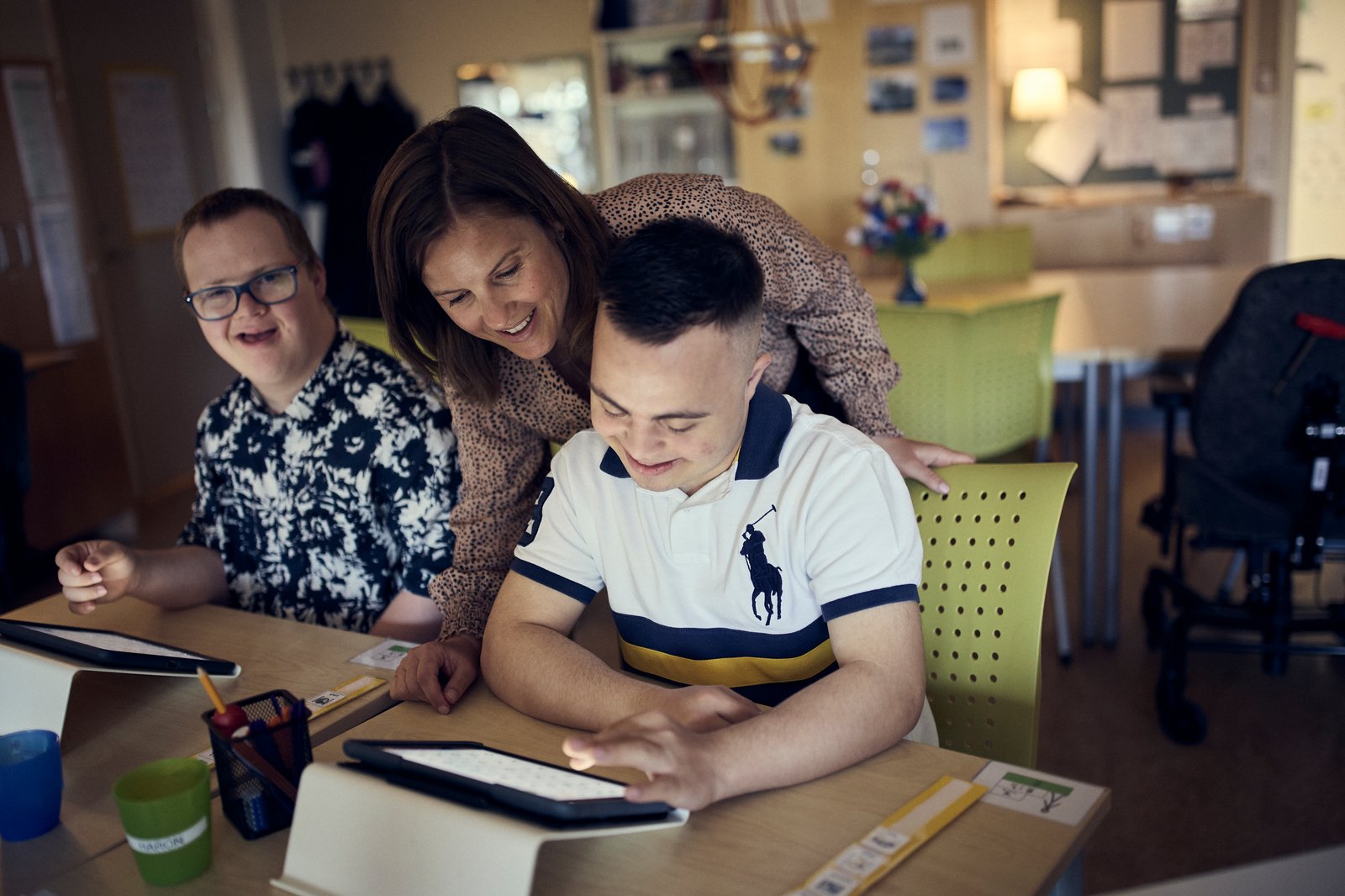 Två elever sitter vid ett bord och jobbar med sina ipads och får hjälp av sin lärare. 