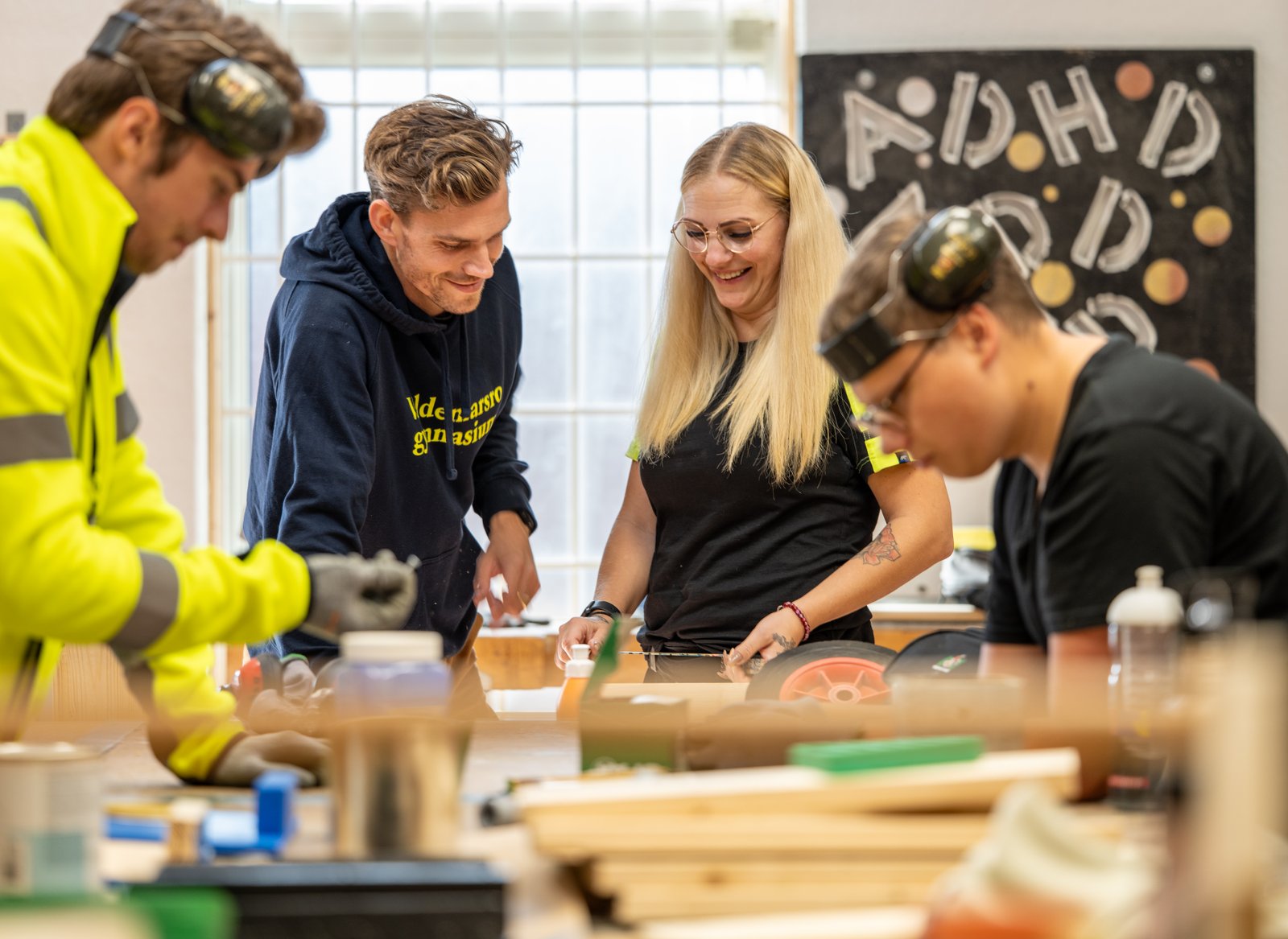 Två elever och två lärare befinner sig i en verkstad. 