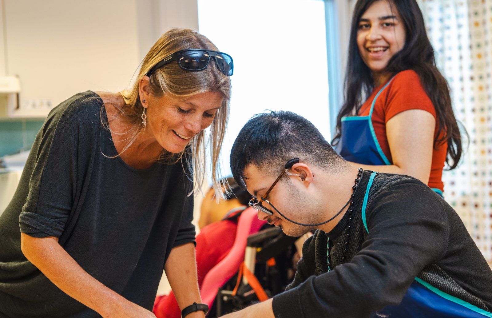 En lärare tillsammans med två elever. Ena eleven ler in i kameran. 