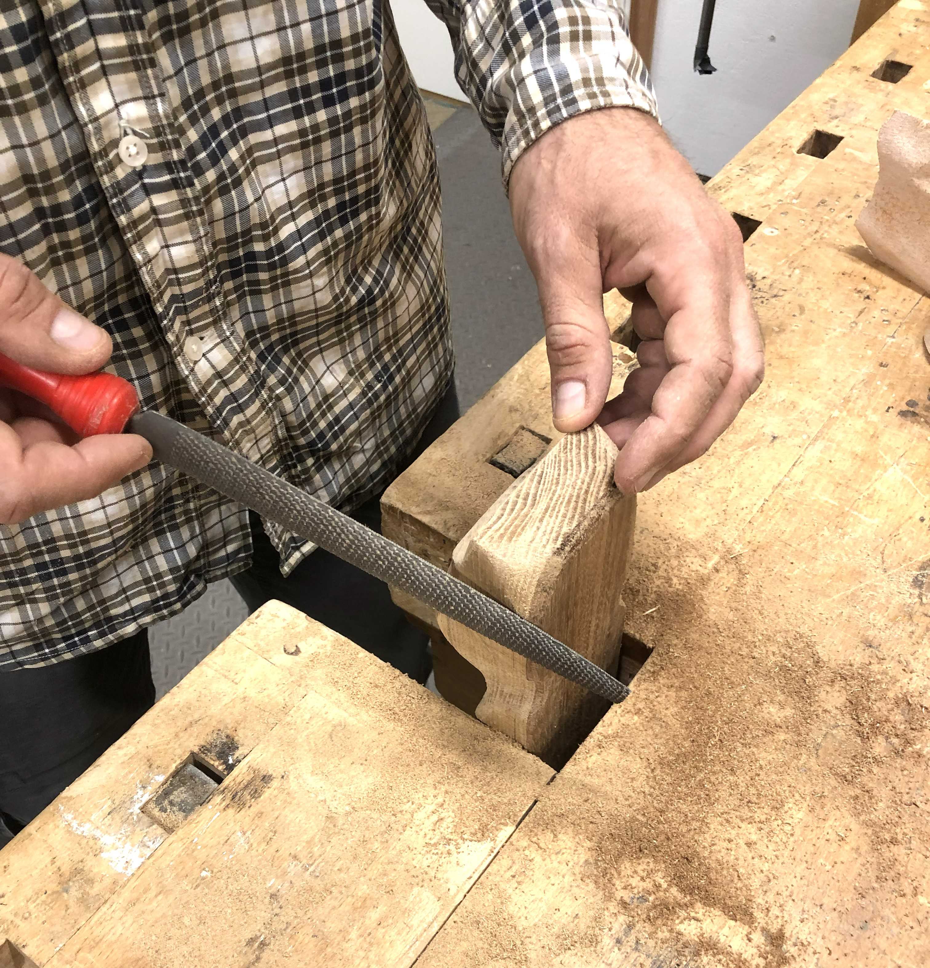 En person står och filar en träbit.