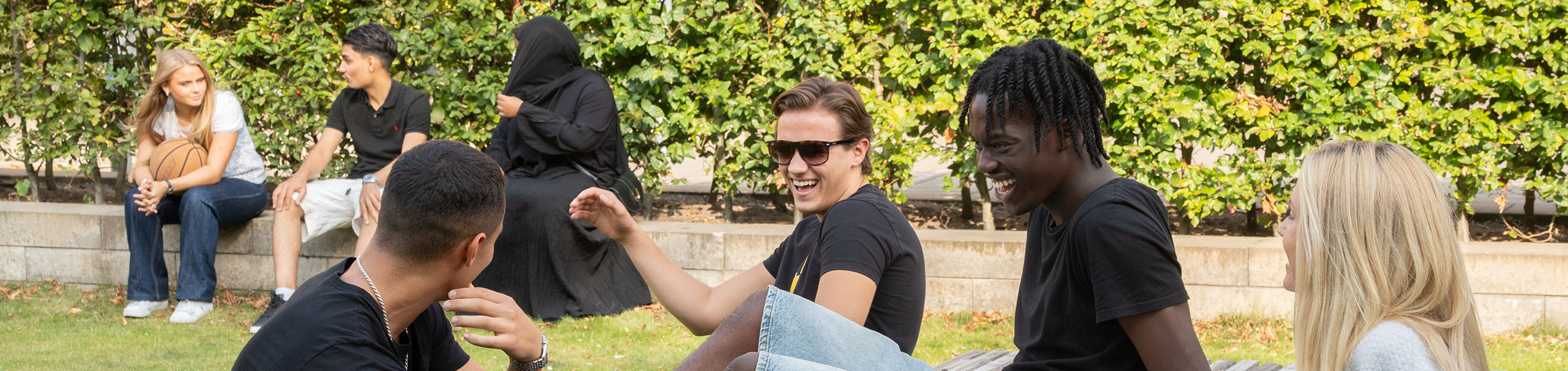 Sju elever sitter och pratar på en grönskande skolgård.