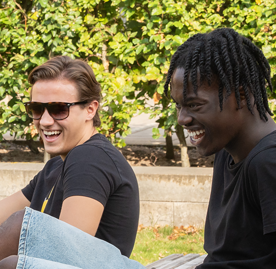 Två elever sitter utomhus. De skrattar.