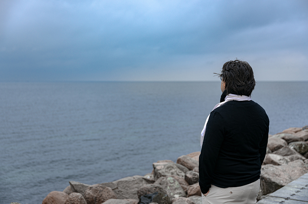 Chias står med ryggen mot kameran, med händerna i byxfickorna, och blickar ut mot havet