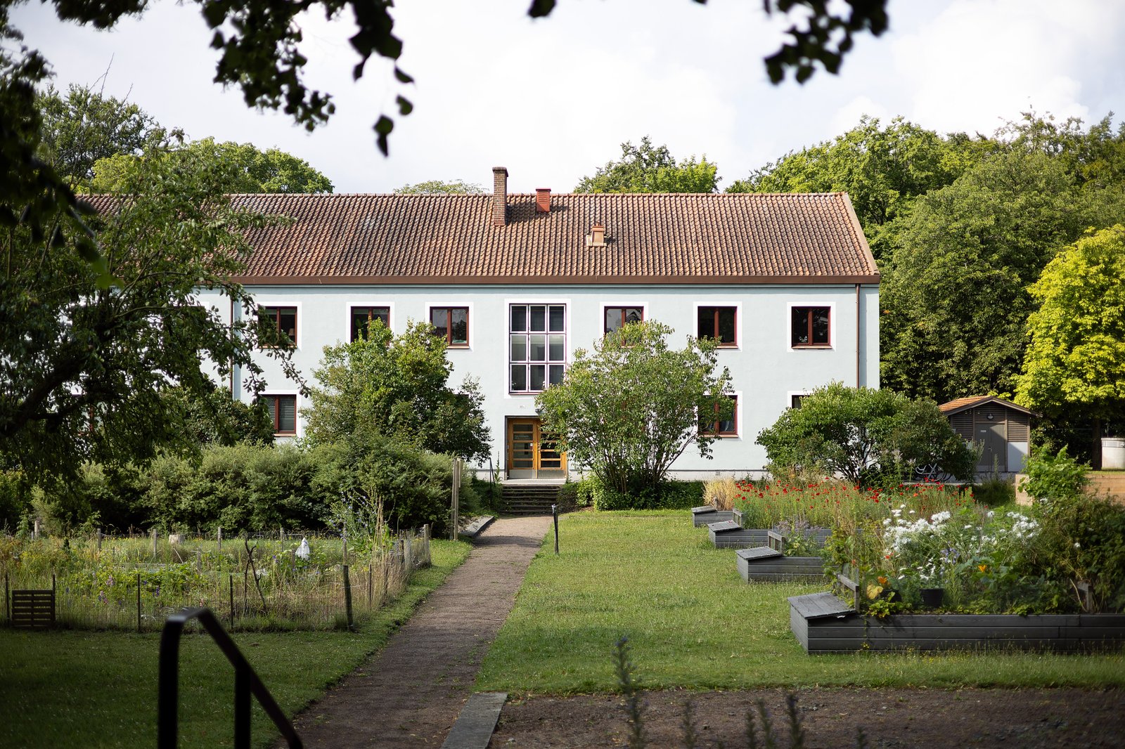 Blått hus från 30-talet bland grönskande träd och buskar