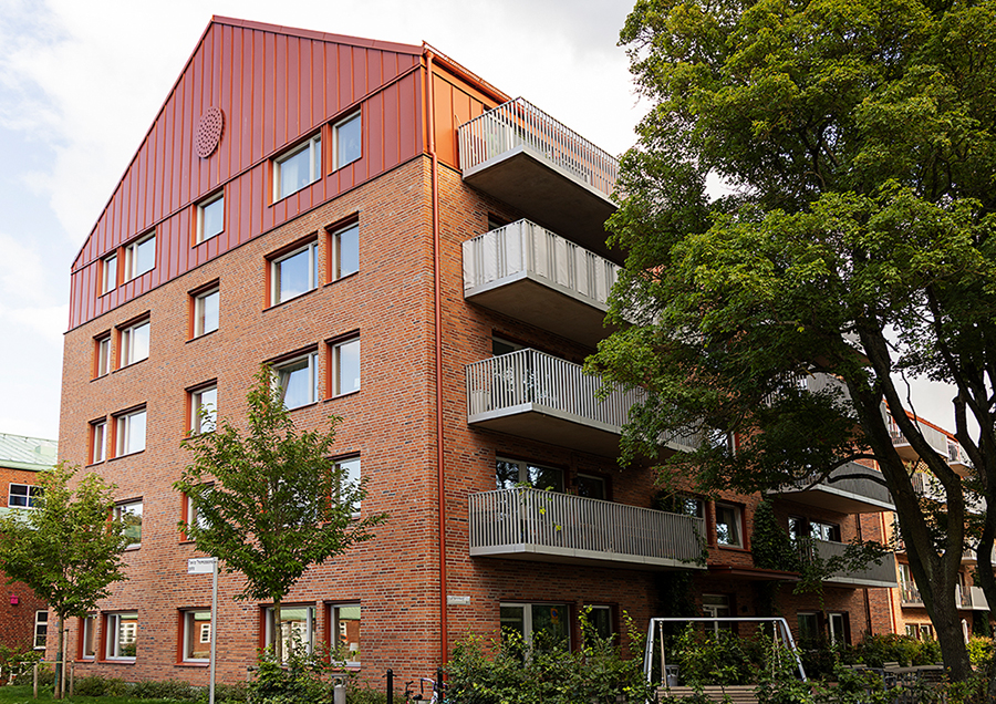 Bild på ett högt hus i tegel med flera balkonger och ett stort träd