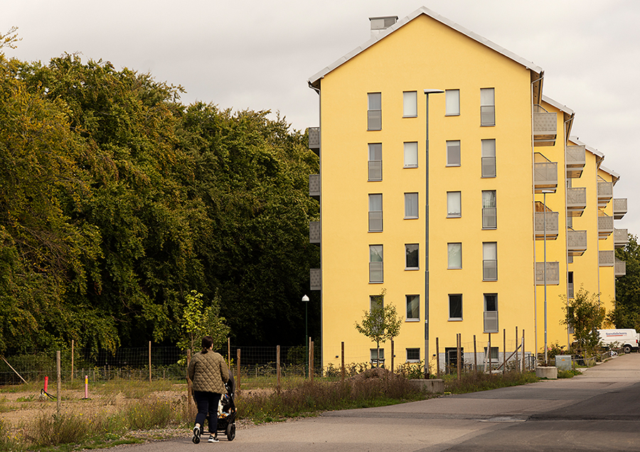 Ljusgult flerbostadshus. Ljusblå himmel bakom och grönska i bildens ena hörn.