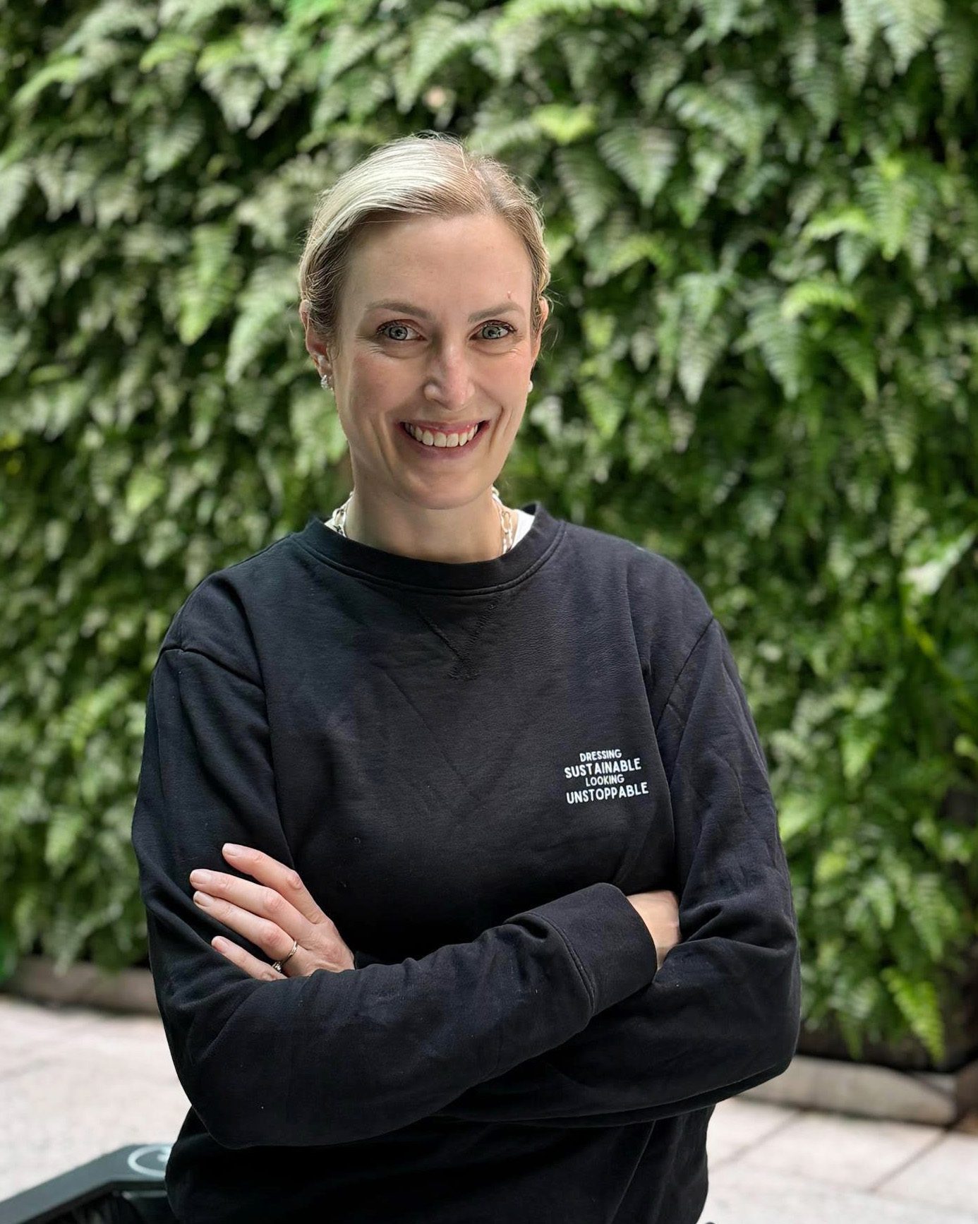 En kvinna med en svart tröja står med armarna i kors, tittar in i kameran och ler.